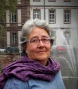 Portrait Dr. Marceline Naudi wearing a purple scarf standing in front of a building